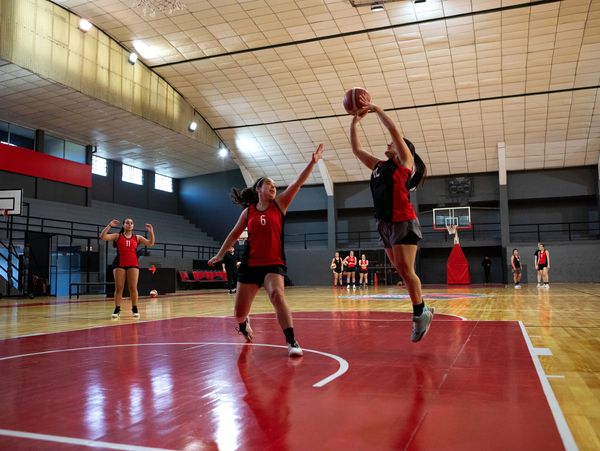 Women’s basketball players competing on an indoor court, one shooting and one defending