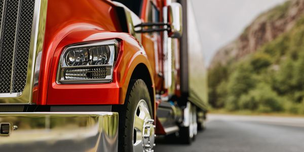 Close-up of a shiny red semi-truck on a road near green hills.
