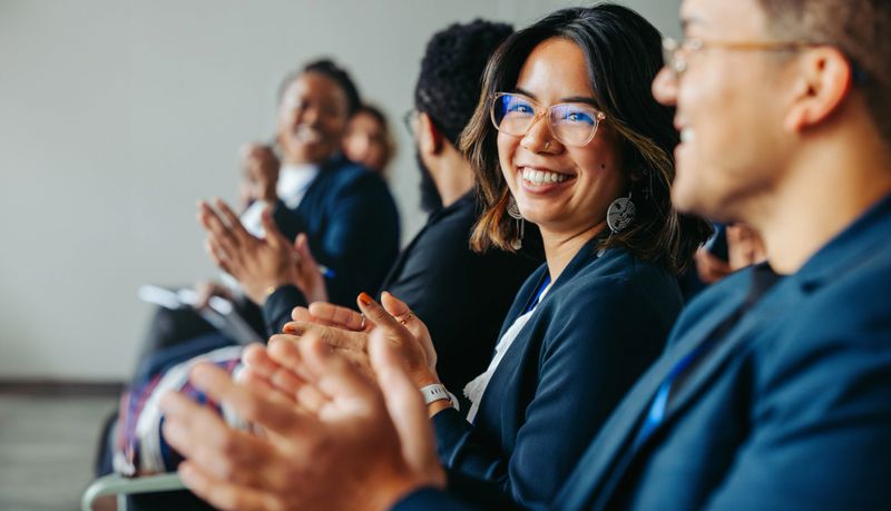 Group of diverse colleagues clapping and smiling happily during a business meeting, showcasing teamwork and positive workplace atmosphere.