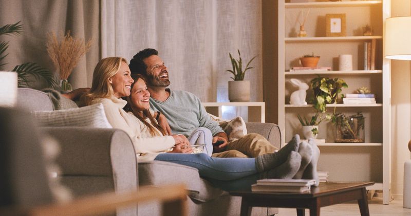 Family, watching tv and laugh in living room for weekend, movies and comedy or comfort in home. Mother, father and teenager or girl on couch for television, film or subscription for streaming on sofa