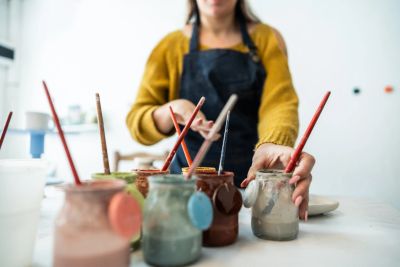 Person reaching for a paintbrush among jars of paint in a studio.