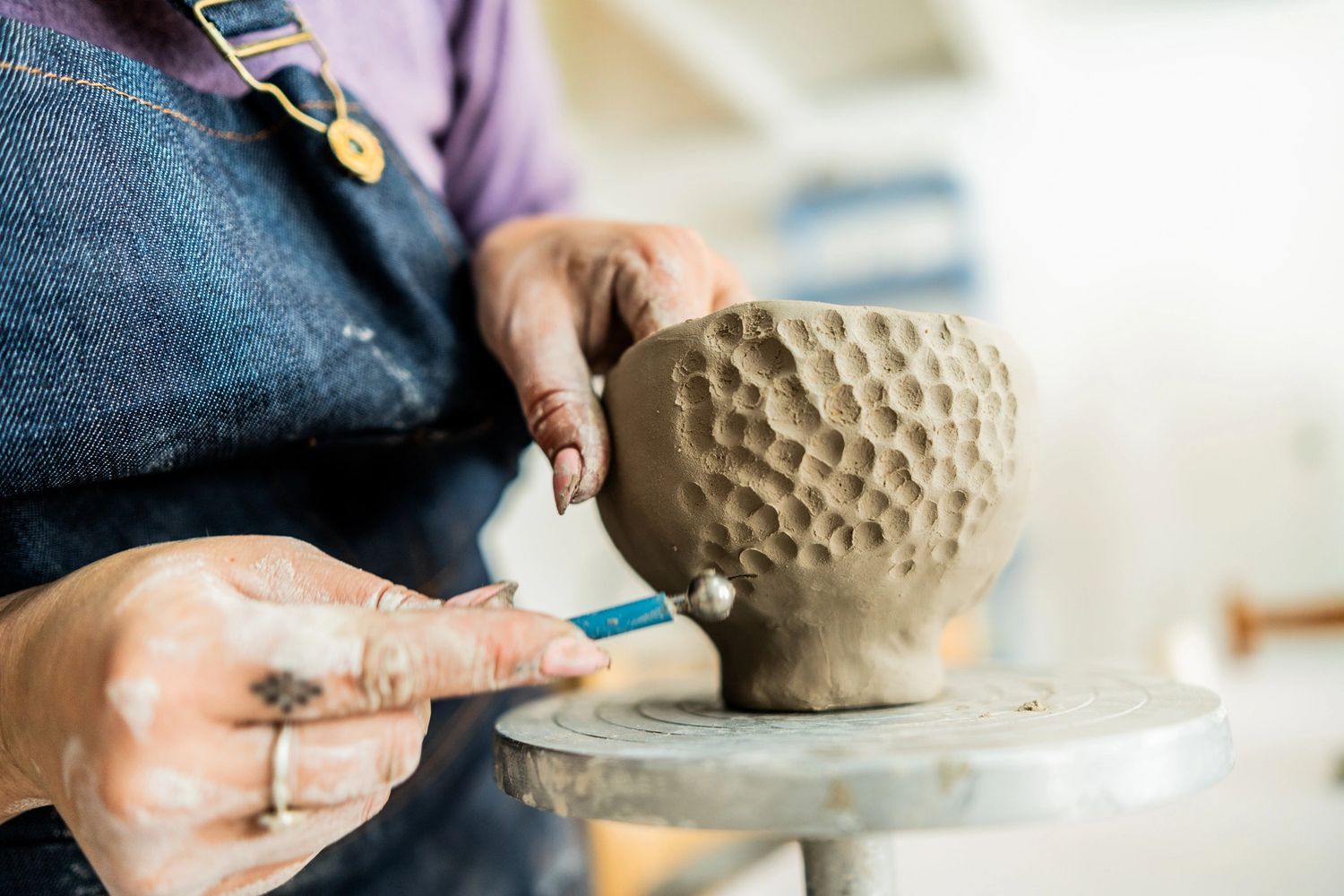 A person sculpting a textured clay bowl on a pottery wheel.