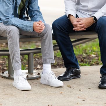Two people sitting on a bench with hands clasped, wearing casual and formal shoes.
