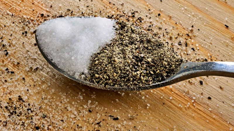 close up of a spoon filled with salt and pepper