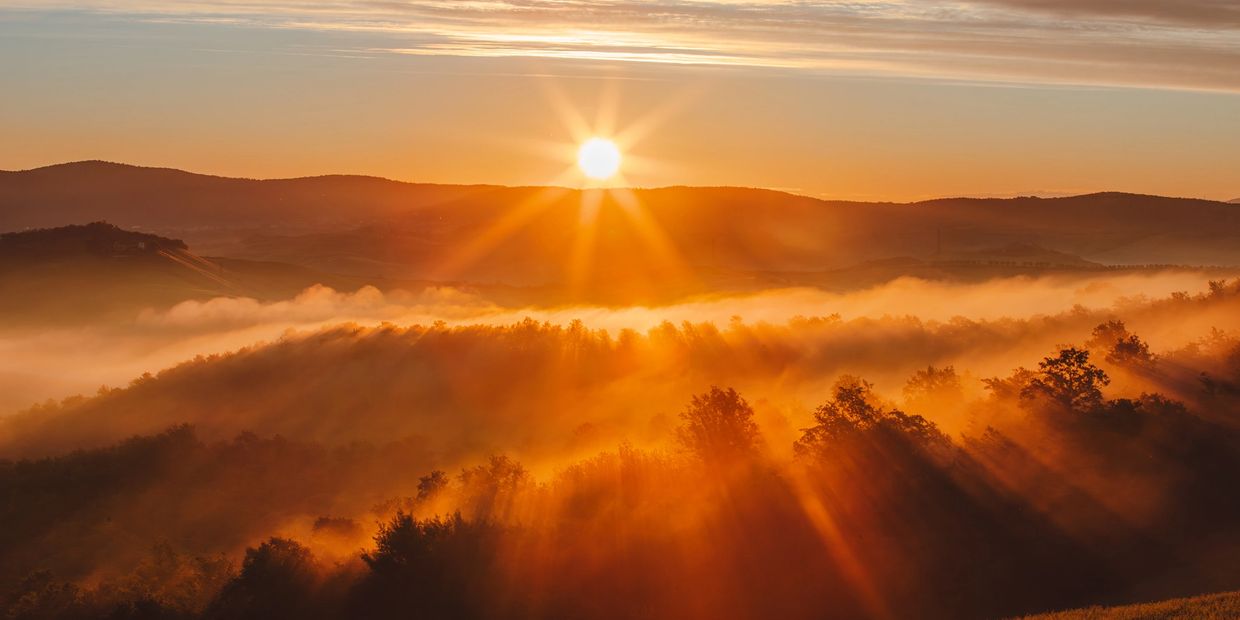 Sunrise over misty hills casting golden rays.