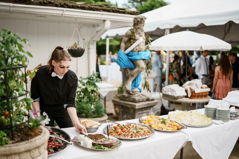 A female event manager sets up a table of delicious food for a wedding reception of a male gay couple.