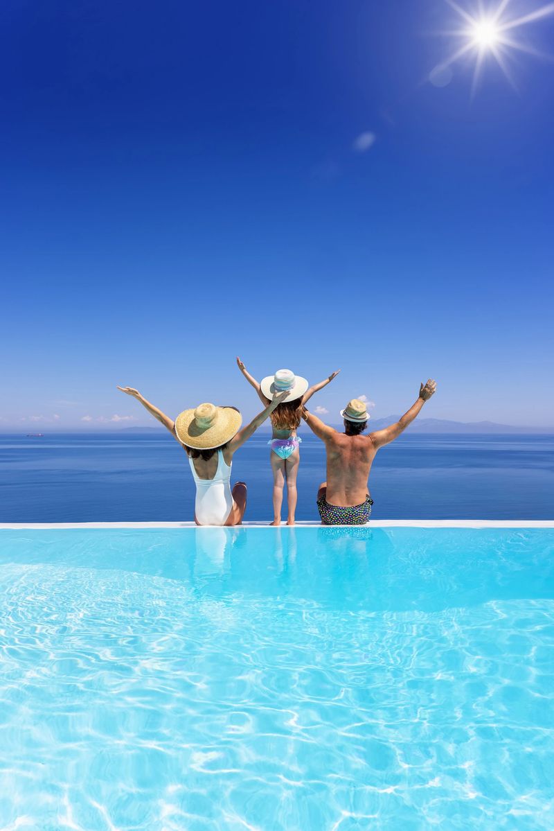 A happy family on summer holidays sits by the swimming pool and enjoys the beautiful view