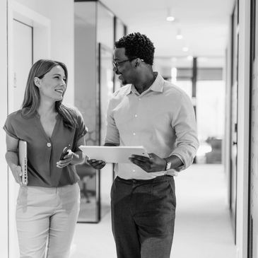 Two colleagues walking and talking in a modern office hallway.