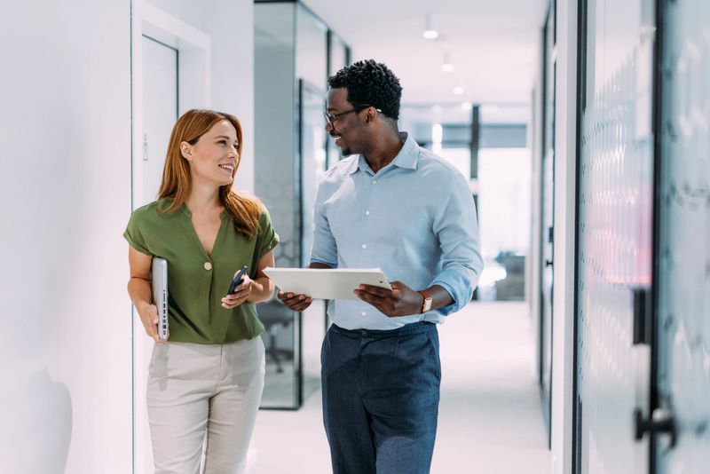 Shot of two coworkers having a discussion in modern office. Businessman and businesswoman in meeting discussing important financial documents. Confident business people working together in the office. Corporate business persons discussing new project and sharing ideas in the workplace.