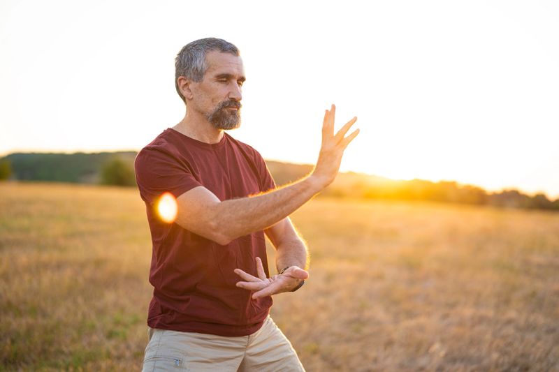 Tai Chi health benefits. Active mature man out in nature at sunset doing relaxing movements to achieve mental and physical harmony. Self-improvement concept.