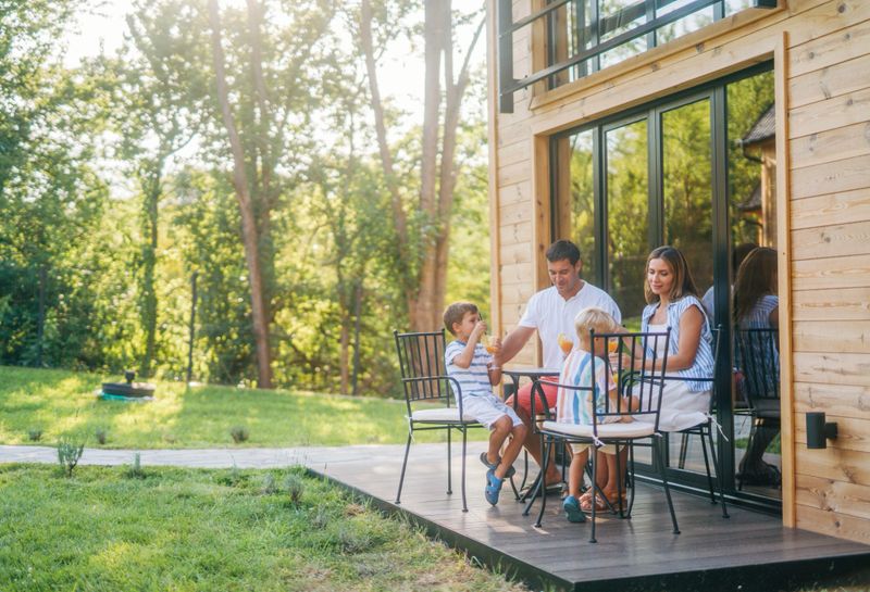 A family of four, consisting of a mom, dad, and their two sons, is spending quality time together on a sunny day. They are seated around a table on the patio of their vacation home.