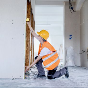 Trabajador con casco mide una pared interior.