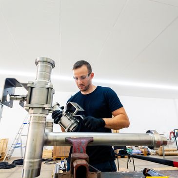 Technician assembling a large metal pipe system in a workshop.