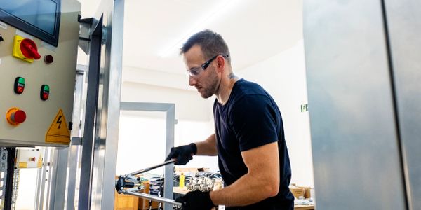 Technician operating industrial equipment with safety glasses and gloves.