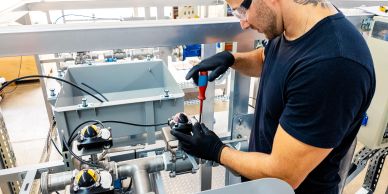 Technician repairing industrial equipment with a screwdriver.