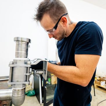Man wearing safety glasses working on industrial machinery indoors.