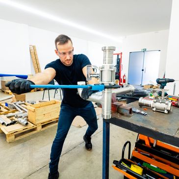 A man uses a large wrench to tighten a metal pipe in a workshop.