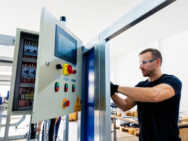 A technician working on an industrial control panel in a factory setting.