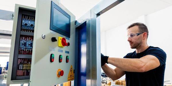 A technician working on an industrial control panel in a factory setting.