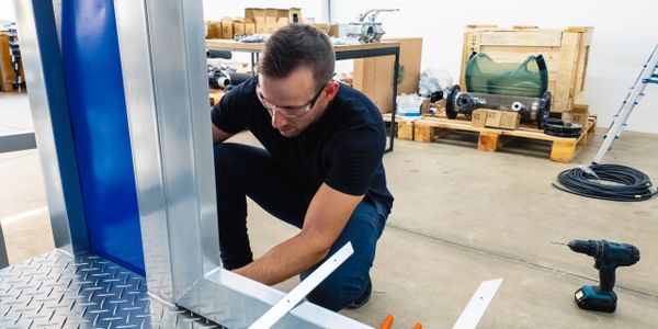 Man wearing safety glasses working on metal structure in workshop.