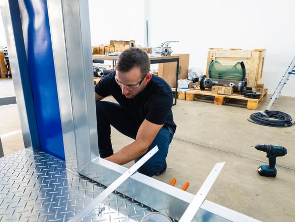 Man wearing safety glasses working on metal structure in workshop.