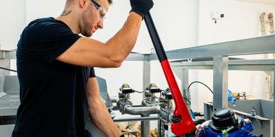 A technician uses a large wrench to adjust industrial piping.