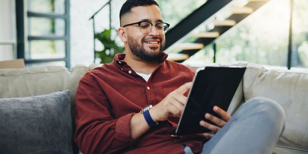 Man smiling while using a tablet on a couch.
