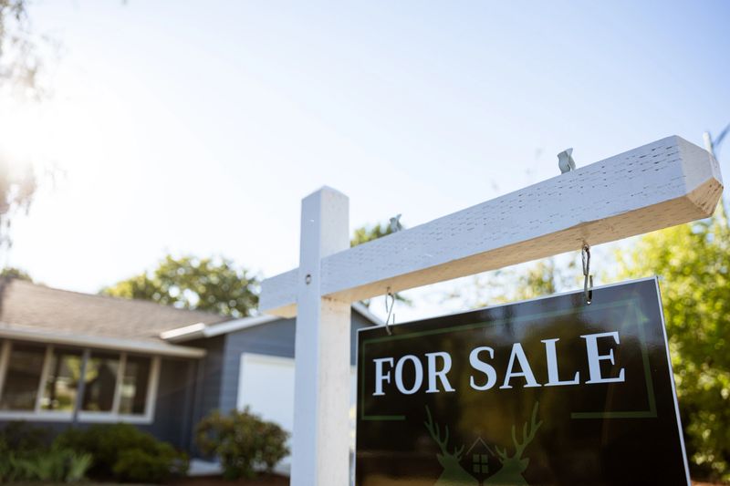 Image of a real estate for sale sign posted in front of a residential home in Portland Oregon. Shot from the street with sun as back light.