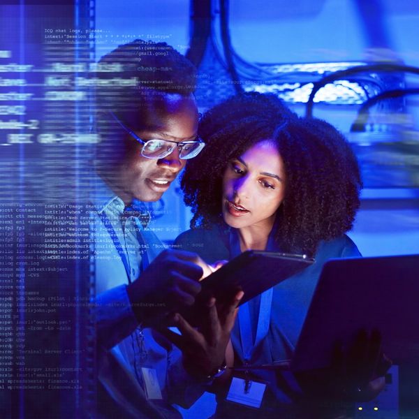 Two professionals analyzing data on a tablet in a tech environment with blue digital overlay.