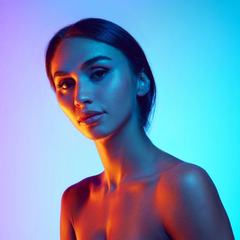 Beautiful young woman with dark hair in ponytail, tanned skin and clear, spotless face against gradient background in neon light. Concept of beauty, skin and body care, cosmetology and cosmetics