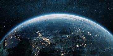 A nighttime view of Earth from space showing illuminated cities and starry sky.