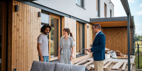 A couple and a real estate agent discussing a wooden deck outside a modern house.