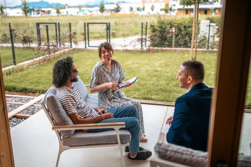 A diverse couple sits outdoors with bright smiles, signing paperwork with a professional real estate agent, marking a new chapter in homeownership.