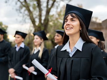 Happy graduates in caps and gowns holding diplomas outdoors.