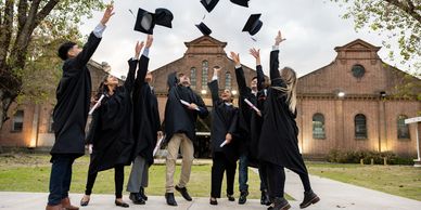 Graduates in black gowns toss caps outdoors in celebration.