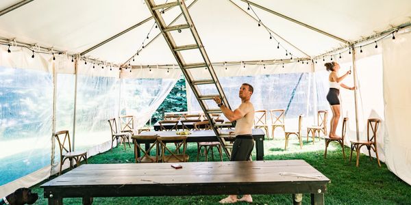 Image shows the setting up of party tent by two people with a ladder.
