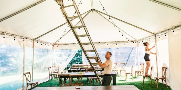 Two people setting up lights inside a tent.