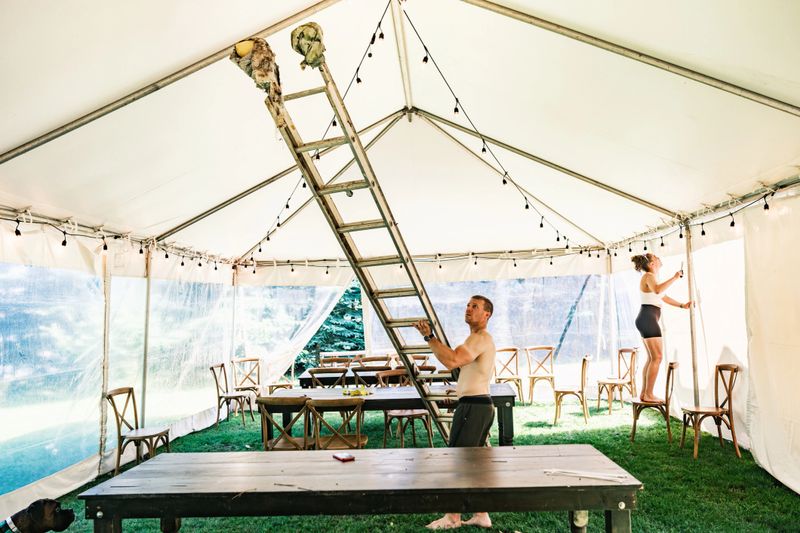 Young couple decorating lights inside wedding reception tent. Both dressed in summer sport outfits. Exterior of  party tent in cottage country in Muskoka, Ontario in Canada.
