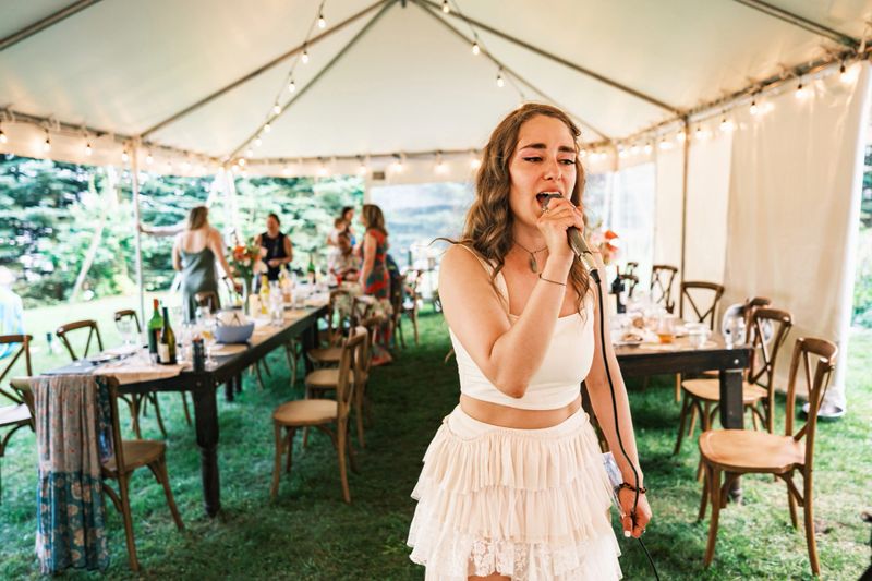 Bride singing karaoke at the wedding party. People in the background. Exterior of  party tent in cottage country in Muskoka, Ontario in Canada.