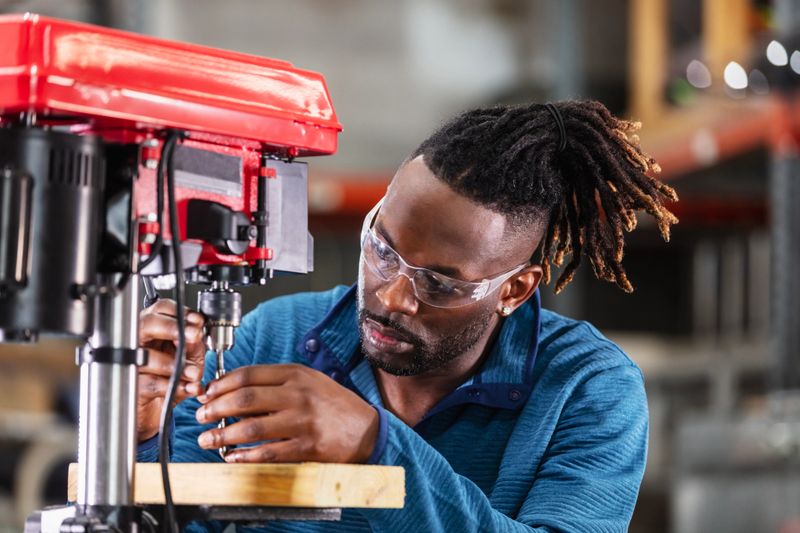 Close-up of an African-American man putting a bit in a drill press. He is a skilled worker in a small factory.