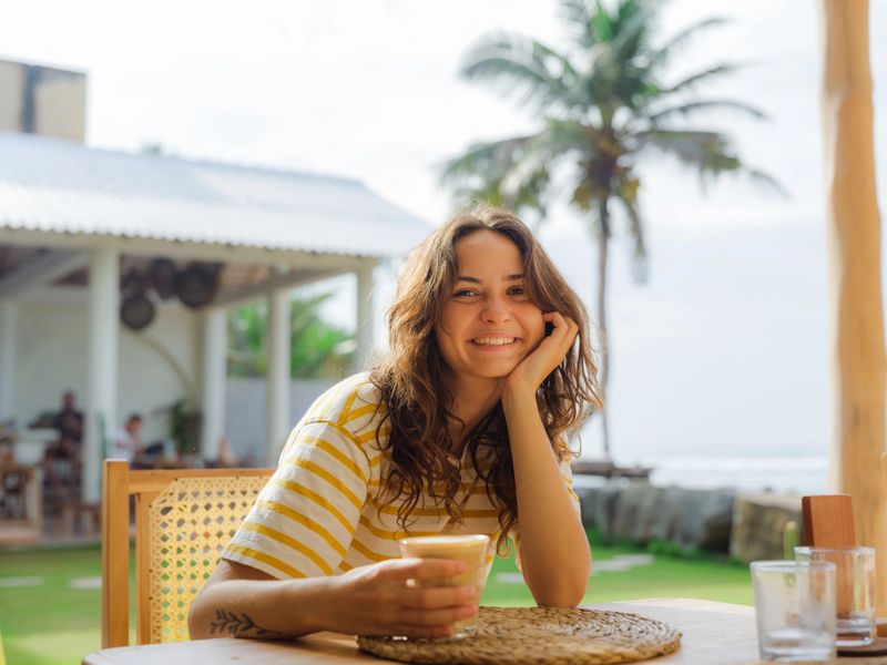 Portrait of woman  drinking coffee in cafe at the beach under the palm tree during vacation