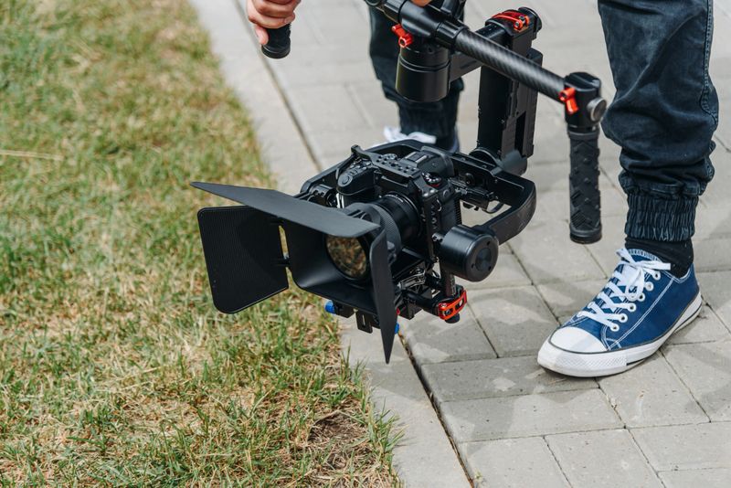 videographer working outdoors in park with video camera set on steadycam, cameraman at work