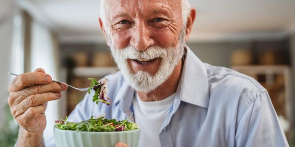 Smiling elderly man enjoying a fresh salad at home.