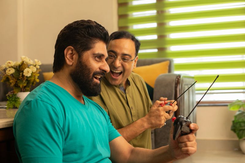 Excited adult male friends playing video game with joysticks while spending weekend together in living room