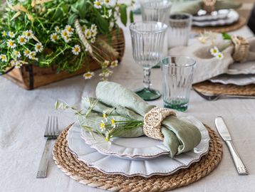 Elegant table setting with green napkins and fresh flowers on woven placemats.