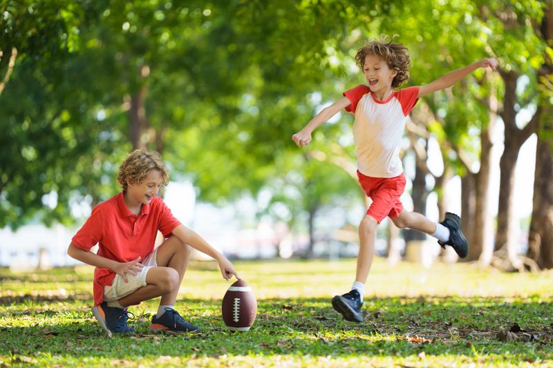 Family playing American football. Kids play rugby in sunny summer park. Father and children throw ball, run and laugh. Healthy outdoor sport activity.