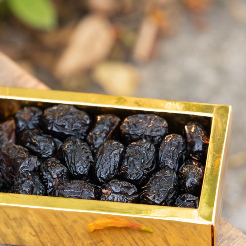 Golden box filled with dried dates placed outdoors, highlighting the rich, dark color and wrinkled texture of the dates.