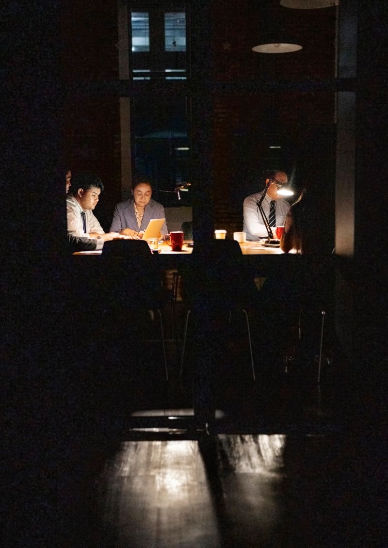 Low light shot of team of business professionals working overtime on laptop late at night to complete a project before the deadline