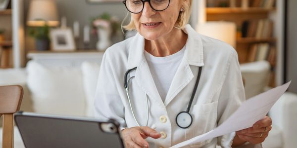 Female doctor consulting via video call with documents in hand.