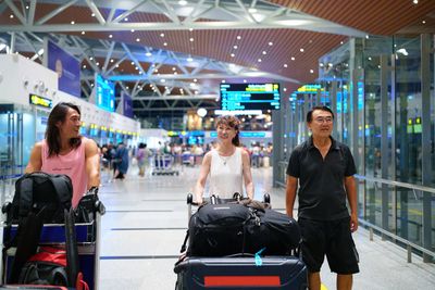 Three people smiling with luggage carts in an airport terminal.